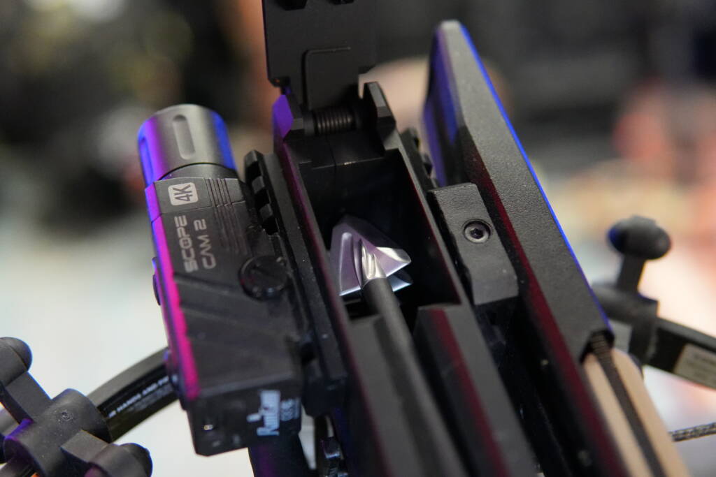 Crossbow rail close-up with loaded bolt and broadhead, showing scope and arrow retention system in detail