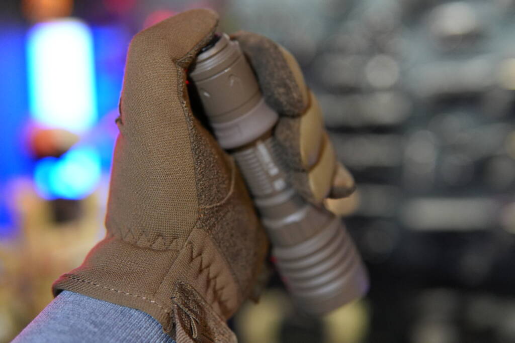 Olight Warrior X4 tactical flashlight operated via rear tail switch while wearing tactical gloves.