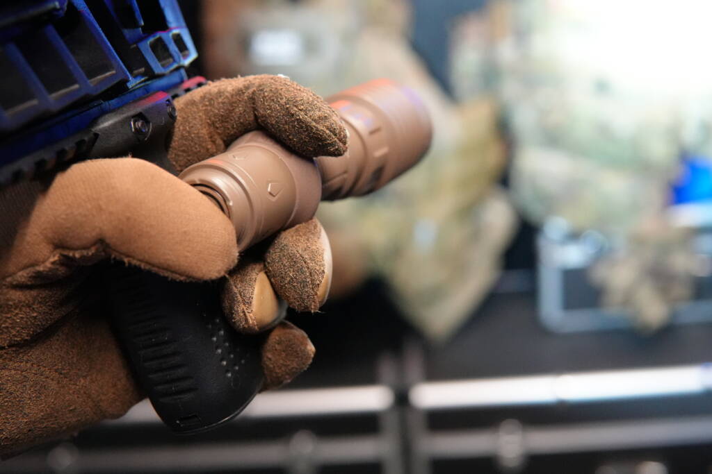 Handheld Olight Warrior X4 tactical flashlight used alongside a firearm, not mounted to the weapon.