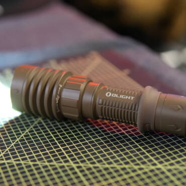 Olight Warrior X4 tactical flashlight turned on and lying on a workbench, emitting bright white light.