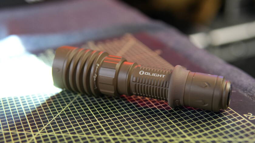 Olight Warrior X4 tactical flashlight turned on and lying on a workbench, emitting bright white light.