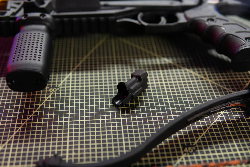 Projectile sled for the Steambow B08 less-lethal crossbow placed on a cutting mat, with the lower receiver grip and CQ limb blurred in the background.