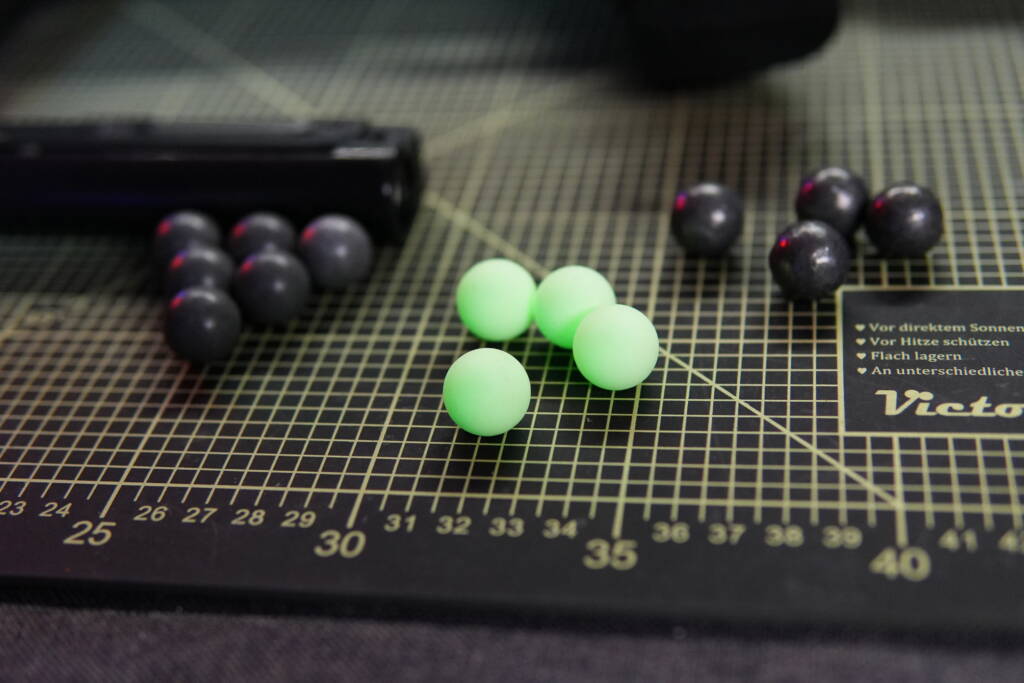 Various .68 caliber projectiles for the Steambow B08, including UV-charged glowing T4E tracer balls emitting green light on a cutting mat.