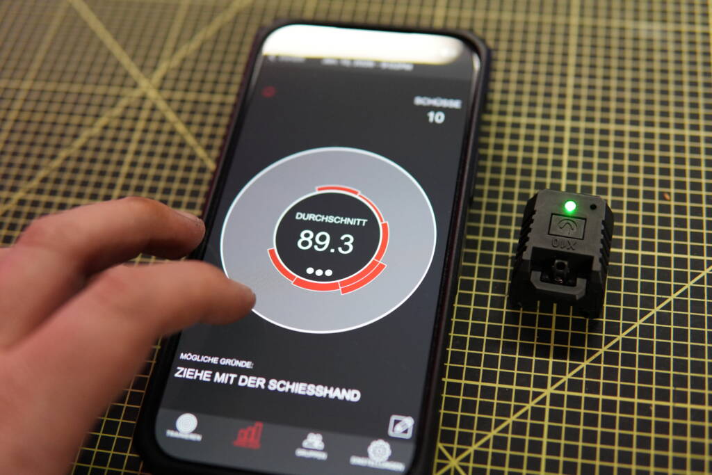 Mantis X10 shooting analysis displayed on an iPhone with the connected sensor placed beside it on a workbench.