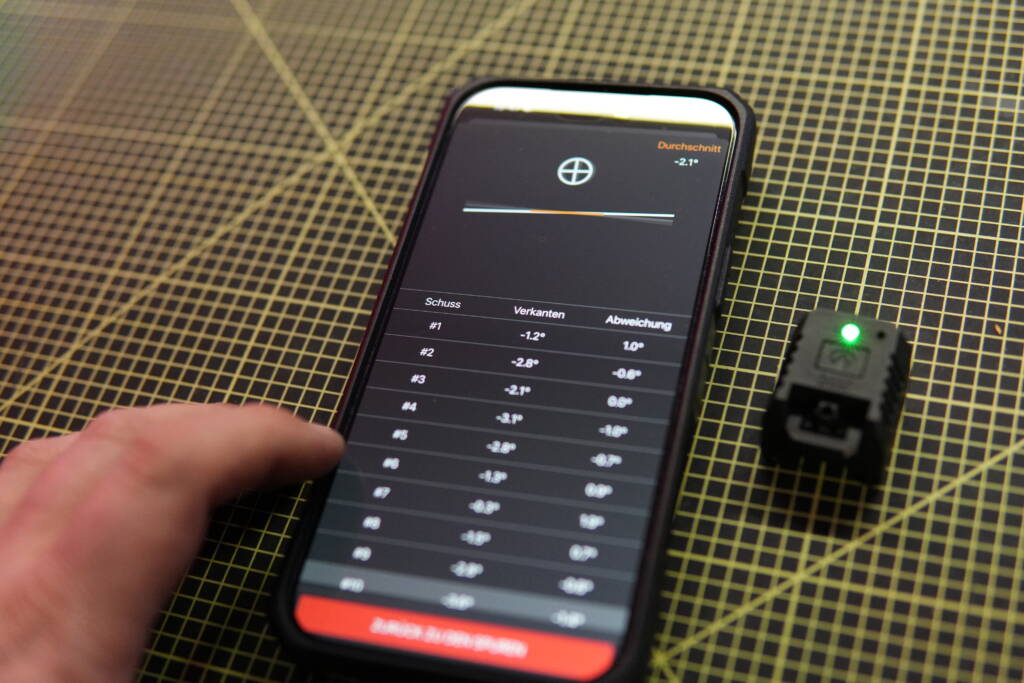 Mantis X10 cant analysis displayed on a smartphone showing shot-by-shot tilt data with connected sensor beside it.