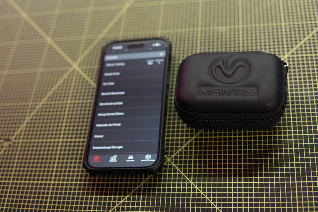 Mantis X10 protective carrying case next to a smartphone displaying the Mantis app challenge menu.