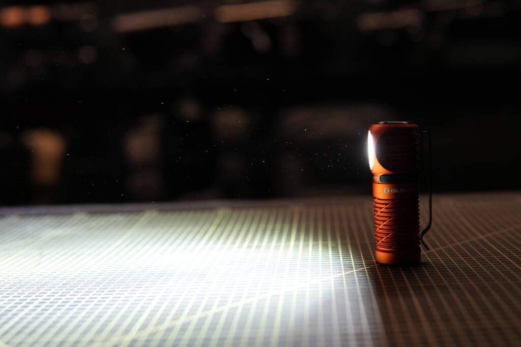 Olight Perun 3 Mini standing upright in a dark room, brightly illuminating the entire space.