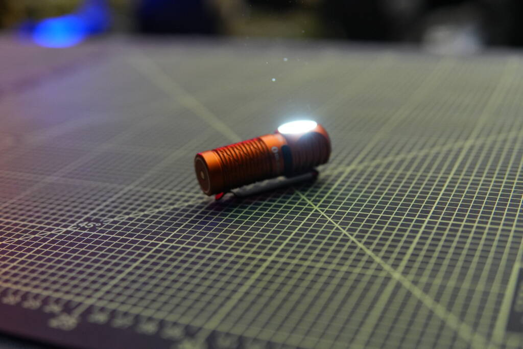 Olight Perun 3 Mini turned on and shining upward with medium brightness on a cutting mat.