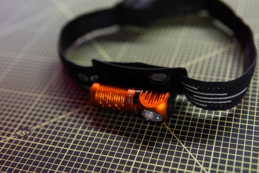 Olight Perun 3 Mini mounted on headband with visible quick-release button for fast detachment.