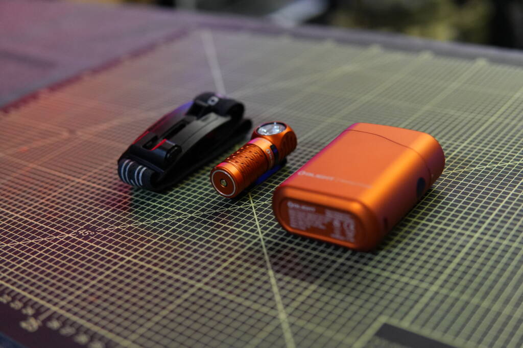 Olight Perun 3 Mini with headband and orange charging case that also functions as a power bank on a cutting mat.