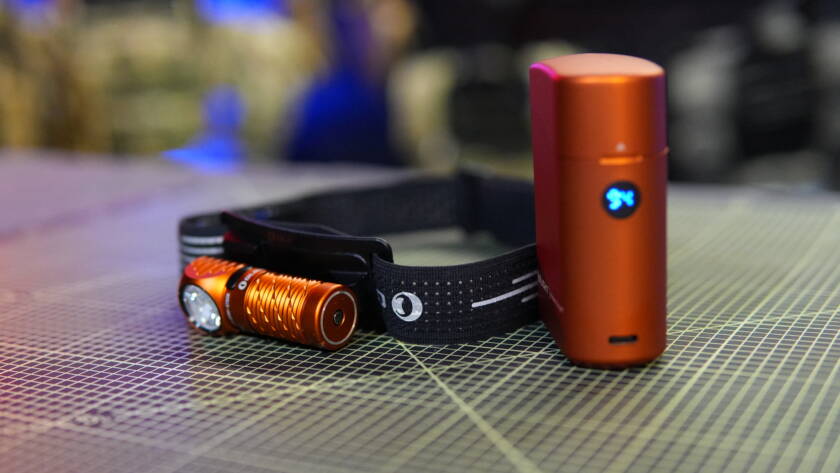 Olight Perun 3 Mini headlamp mounted on headband with orange charging case placed beside it on a cutting mat.