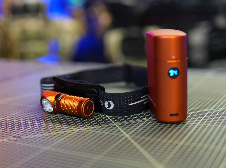 Olight Perun 3 Mini headlamp mounted on headband with orange charging case placed beside it on a cutting mat.
